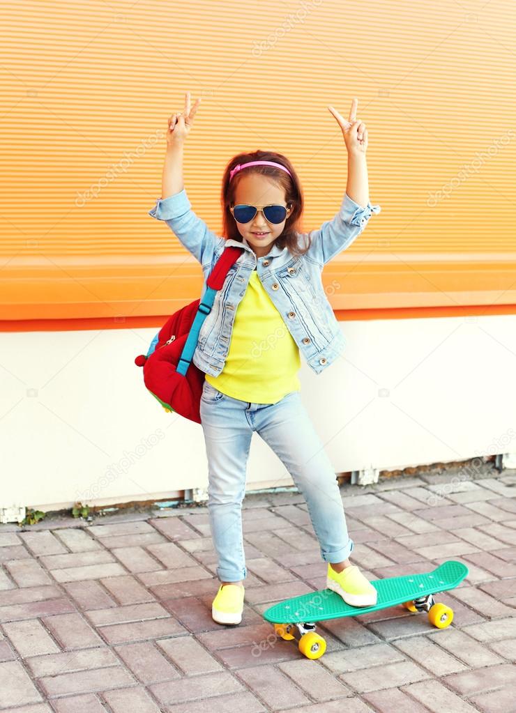 Stylish little girl child with skateboard having fun in city ove