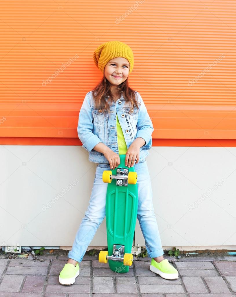 Stylish little girl child with skateboard having fun in city