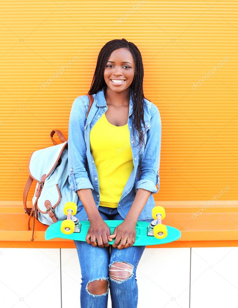 Beautiful smiling african woman with skateboard over colorful or