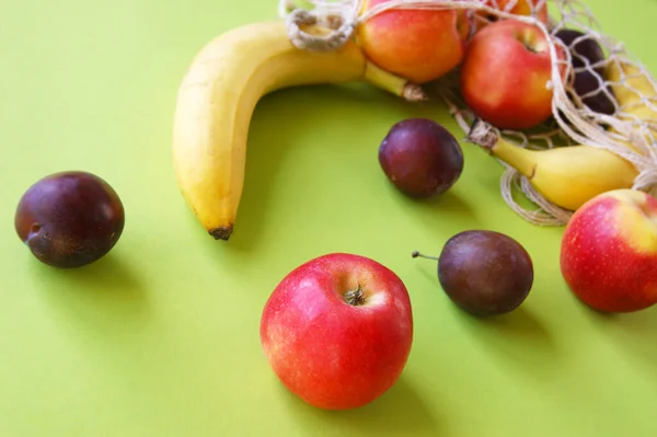 Maçãs Vermelhas Bananas Ameixas Saco Cordas Fundo Verde Brilhante Frutas — Fotografia de Stock