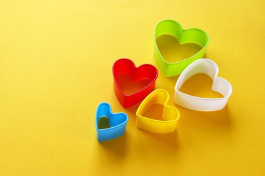 Sarı arka planda kalp şeklinde kurabiyeler yapmak için çok renkli plastik kalıplar. Mutfak ya da parti konsepti. Boşluğu kopyala.