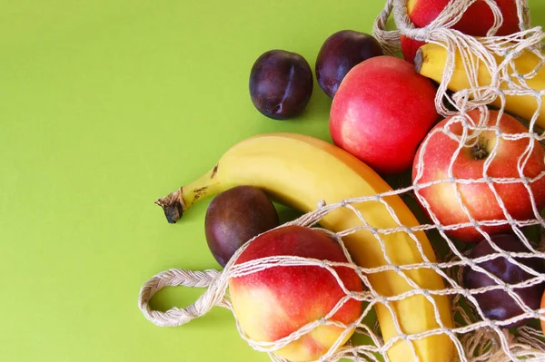 Maçãs Vermelhas Bananas Ameixas Saco Cordas Fundo Verde Brilhante Frutas — Fotografia de Stock