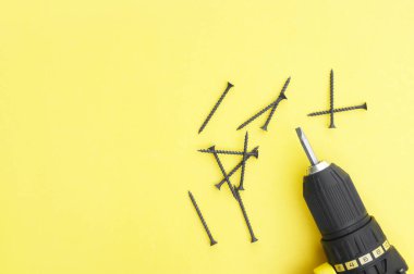 Sarı arka planda sarı-siyah tornavida, vidalar.