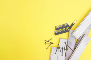 Kendi kendine dokunan vidalar, birkaç parça ve sarı arka planda tahta tahtalar. Metne yer var..