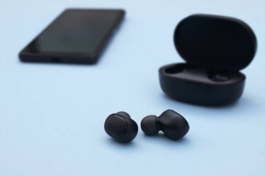 Akıllı telefon, kablosuz kulaklık ya da parlak mavi arka planda şarj çantası olan kulaklık. Müzik teknolojisi eğilimleri 2020-2021.