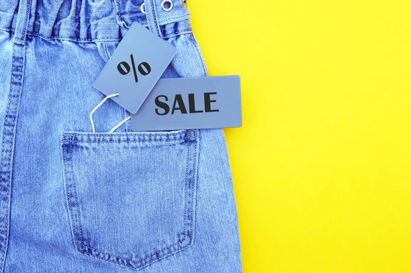 蓝色牛仔裤的细节与灰色标签和题词Sale的黄色背景 购物和打折的概念 黑色星期五 — 图库照片