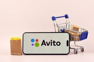 KHARKOV, UKRAINE - 18 Ağustos 2024: Akıllı telefonlu alışveriş arabası beyaz arka planda Avito açık.