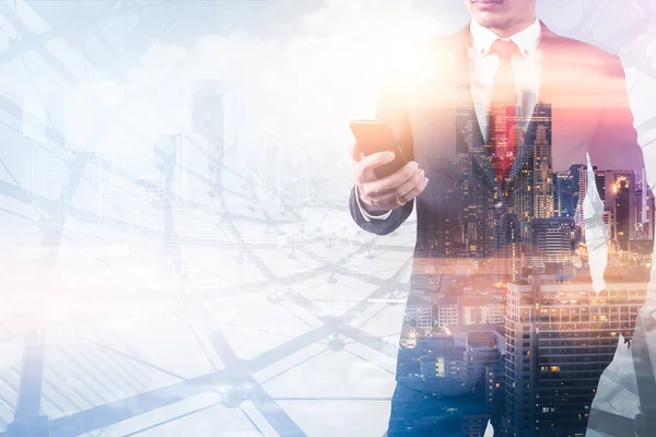 The double exposure image of the businessman using a smartphone during sunrise overlay with a cityscape image. The concept of modern life, business, city life and internet of things.