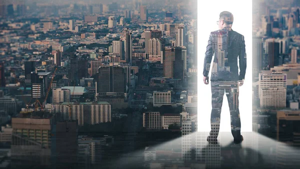 The double exposure image of the businessman standing back during the sunrise overlays with the cityscape image. The concept of modern life, business, city life and internet of things.