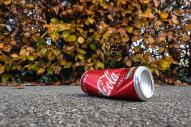 Dietikon, İsviçre - 24 Kasım 2020: Sonbahar renkli bir çitin yanında atılmış ve ezilmiş boş bir Coca Cola kutusu