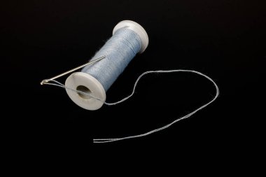 Dikiş aksesuarları: iplik makarası ve siyah arkaplanda bir iğne