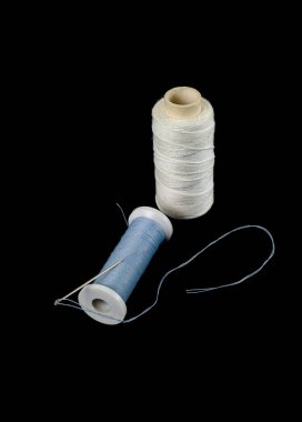 Dikiş aksesuarları: iplik makaraları ve siyah arkaplanda bir iğne