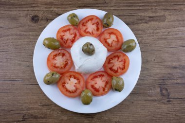 Beyaz tabak ve ahşap masa üzerindeki yemek dilimlenmiş domatesler, çukur zeytinler ve mozzarelladan oluşur.