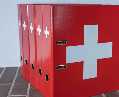 Zürih, İsviçre - 31 Aralık 2020: Ofis ortamında İsviçre bayrağının taklit edilmiş beyaz haçlı kırmızı klasörler