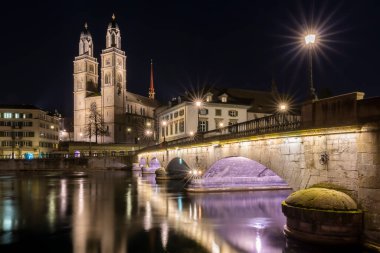 Münih ve Grossmunster Kilisesi geceleri İsviçre 'nin Zürih, Limmat nehrinde yansır.
