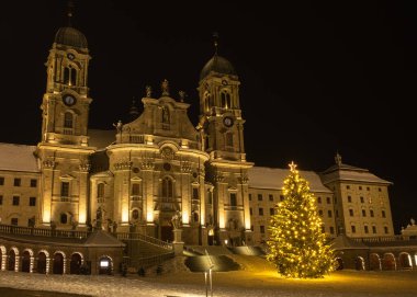 Einsiedeln 'deki Benedictine Manastırı, güçlü bazilikası ile İsviçre' deki ana Katolik hac merkezidir. Noel ağacı ve karlı kış gecesi.