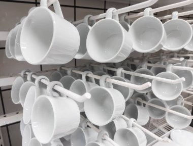 Bir grup beyaz seramik bardak mutfaktaki bir stantta asılı.