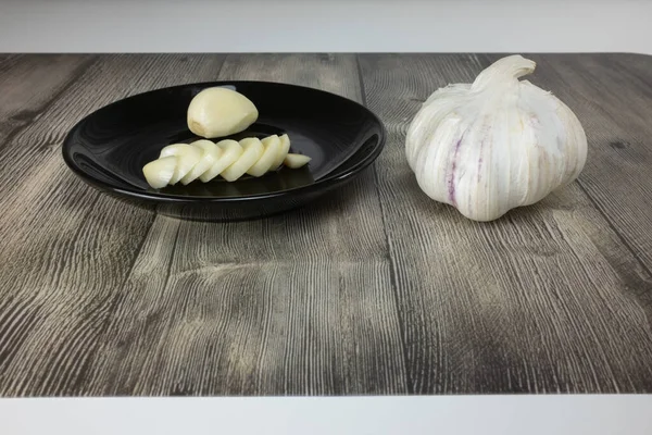 On a black plate is a head of whole garlic and chopped garlic, and next to it a clove of garlic