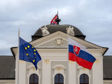 Bratislava, Slovakya - 20 Ekim 2025: Avrupa Birliği ve Slovakya bayrakları başkanlık sarayı önünde heykeller ve bulutlu bir gökyüzü.