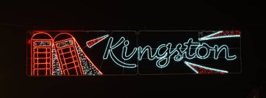 KINGSTON 'u simgesel kırmızı telefon kutuları ve taç motifi ile heceleyen aydınlatılmış dekorasyonların yer aldığı şenlikli bir gece sahnesi..