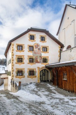 Tarasp, İsviçre - 29 Kasım 2025 Graubunden Tarasp 'taki geleneksel ev renkli duvar resimleri ve ahşap aksanlı, karla çevrili..