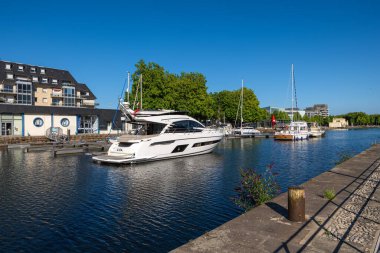 Caen, Fransa - 9 Ağustos 2025: Caen, Normandiya 'daki bir limanın manzaralı manzarası, kırmızı köprüsü, yanaşmış yelkenlileri ve açık mavi gökyüzünün altında suyla kaplı yemyeşil ağaçları.