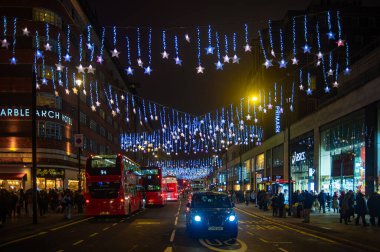 Londra, Birleşik Krallık - 26 Aralık 2025: Londra 'da şenlikli noel ışıkları ve gece kırmızı otobüslerle dolu Oxford Caddesi.