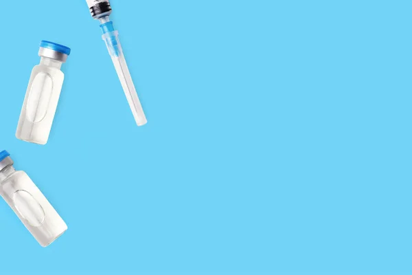 Mavi kapaklı ve şırıngalı iki aşı şişesi. Aşı konsepti. Enjeksiyon kurtarma tedavisi. Coronavirus tıbbi şişesi. Mavi arkaplan, kopyalama alanı.