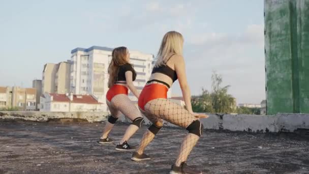 Dos chicas bailan twerk en el techo de un edificio abandonado. Chicas en pantalones cortos rojos y medias a cuadros. — Vídeos de Stock