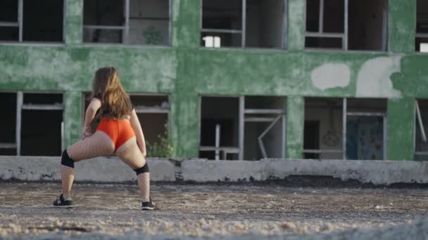 Chica baila twerk en el techo de un edificio abandonado. Chica en pantalones cortos rojos y medias en una celda. — Vídeos de Stock