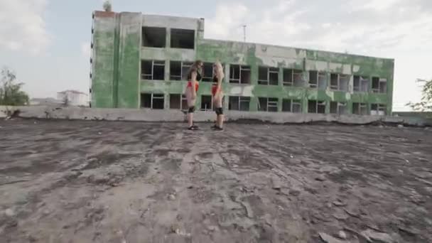 Två flickor dansar twerk på taket till en övergiven byggnad. Flickor i röda shorts och rutiga tights. — Stockvideo