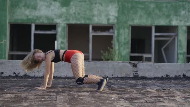 Holka tancuje twerk na střeše opuštěné budovy. Dívka v červených šortkách a punčocháčích v cele. — Stock video
