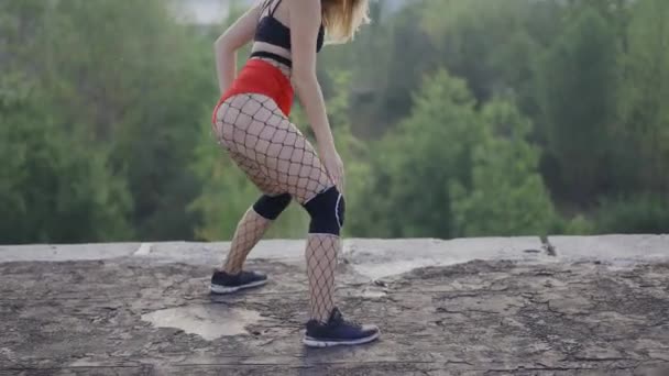 Chica baila twerk en el techo de un edificio abandonado. Chica en pantalones cortos rojos y medias en una celda. — Vídeos de Stock