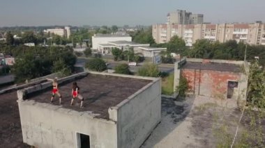 Two girls dance twerk on the roof of an abandoned building. Girls in red shorts and checkered tights. aerial view
