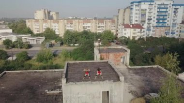 Two girls dance twerk on the roof of an abandoned building. Girls in red shorts and checkered tights. aerial view