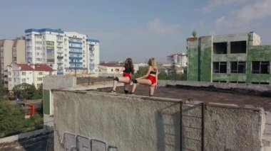 Two girls dance twerk on the roof of an abandoned building. Girls in red shorts and checkered tights. aerial view