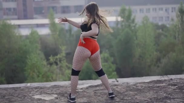 Flickan dansar twerk på taket till en övergiven byggnad. Flicka i röda shorts och trikåer i en cell. — Stockvideo