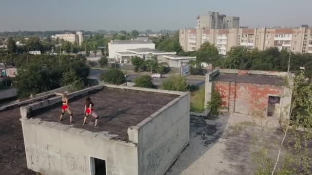 Дві дівчини танцюють на даху покинутої будівлі. Дівчата в червоних шортах і картатих колготках. вид з повітря — стокове відео