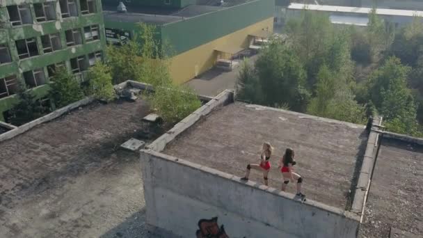 Dos chicas bailan twerk en el techo de un edificio abandonado. Chicas en pantalones cortos rojos y medias a cuadros. vista aérea — Vídeo de stock