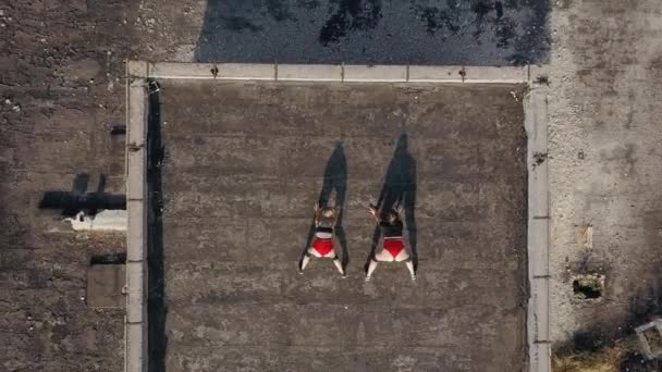 Дві дівчини танцюють на даху покинутої будівлі. Дівчата в червоних шортах і картатих колготках. вид з повітря — стокове відео
