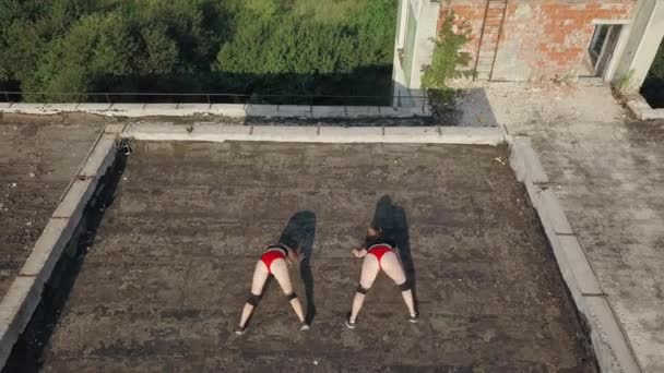 Twee meisjes dansen twerk op het dak van een verlaten gebouw. Meisjes in rode shorts en geruite maillot. vanuit de lucht bekeken — Stockvideo