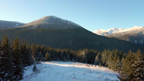 Cuatro viajeros pasan por una gran montaña. La gente conquista los picos nevados de las montañas de invierno. Vista aérea. — Vídeo de stock