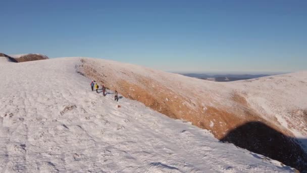 Cuatro escaladores caminan en la cresta de una montaña nevada. La gente conquista las cimas de las montañas de invierno. Vista aérea. — Vídeos de Stock