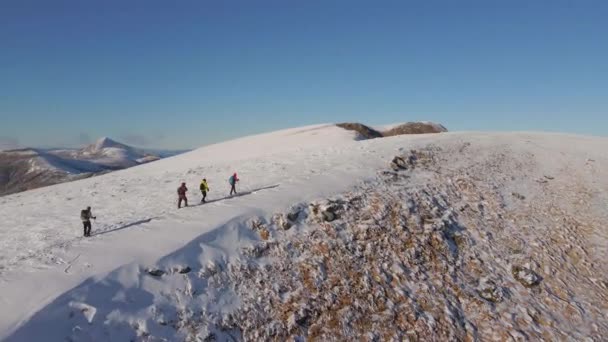 Quattro scalatori camminano sul crinale di una montagna innevata. La gente conquista le cime delle montagne invernali. Vista aerea. — Video Stock