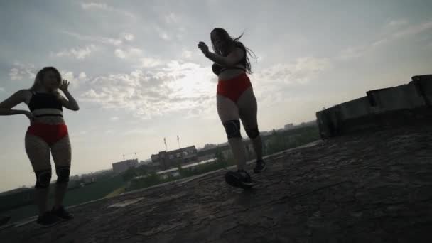 Two girls dance twerk on the roof of an abandoned building. Girls in red shorts and checkered tights. — Stock Video