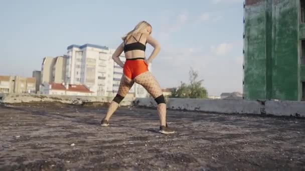 Girl dances twerk on the roof of an abandoned building. Girl in red shorts and tights in a cell. — Stock Video