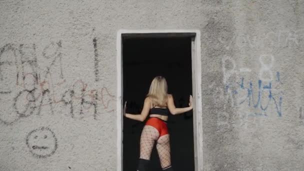 Holka tancuje twerk na střeše opuštěné budovy. Dívka v červených šortkách a punčocháčích v cele. — Stock video