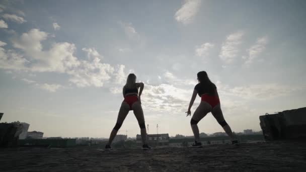 Две девушки танцуют тверк на крыше заброшенного здания. Девушки в красных шортах и клетчатых колготках. — стоковое видео