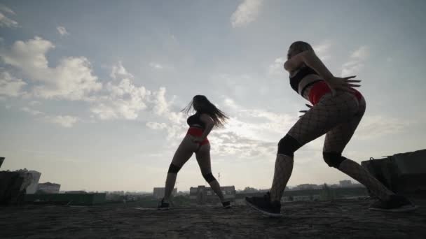 Dos chicas bailan twerk en el techo de un edificio abandonado. Chicas en pantalones cortos rojos y medias a cuadros. — Vídeo de stock
