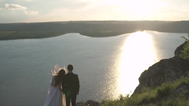 Wind verwischt die Haare der Braut. Bräute stehen am Ufer eines großen Sees. — Stockvideo